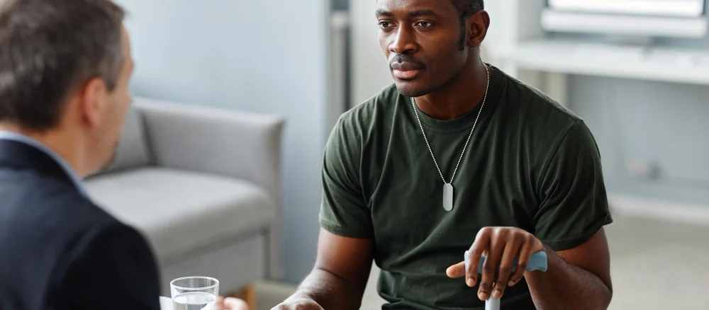 Young adult african american soldier with walking stick talking about his problems to psychologist d