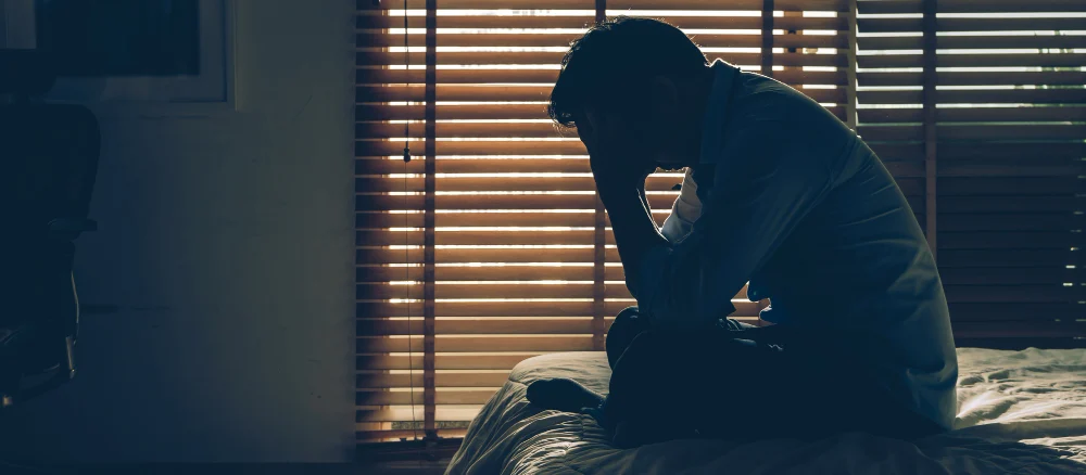 Sad businessman sitting head in hands on the bed in the dark bedroom