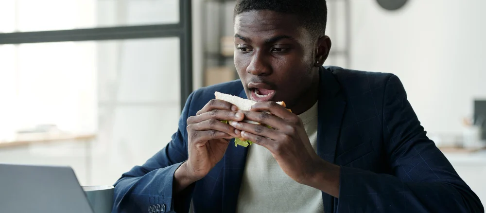 Young hungry office worker in formalwear and eyeglasses eating sandwich