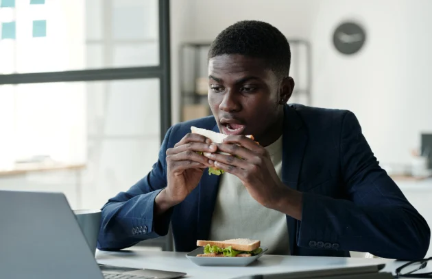 Young hungry office worker in formalwear and eyeglasses eating sandwich