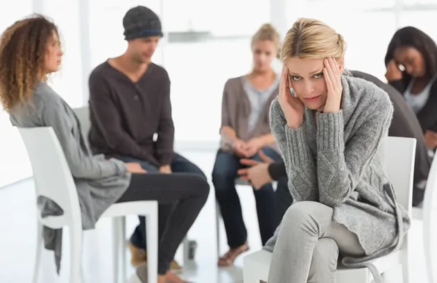 Upset woman with head in hands at rehab group looking at camera
