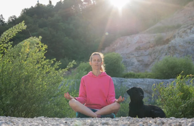 Young woman meditating in nature at sunrise with her dog beside her