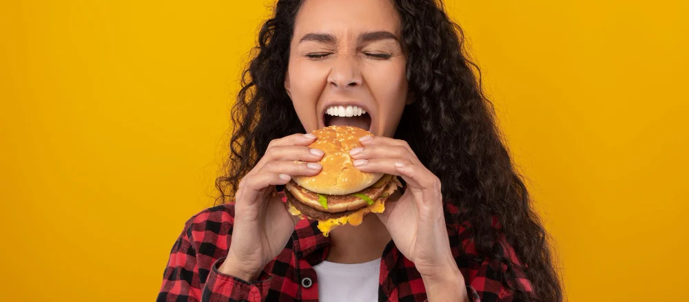 Funny latin lady holding burger biting sandwich at studio