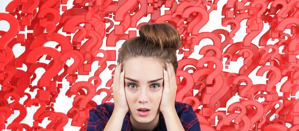 Portrait of a stressed out teen girl sitting against red question marks background. Concept of multiple questions that need to be answered