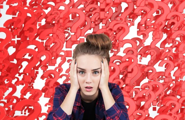 Portrait of a stressed out teen girl sitting against red question marks background. Concept of multiple questions that need to be answered