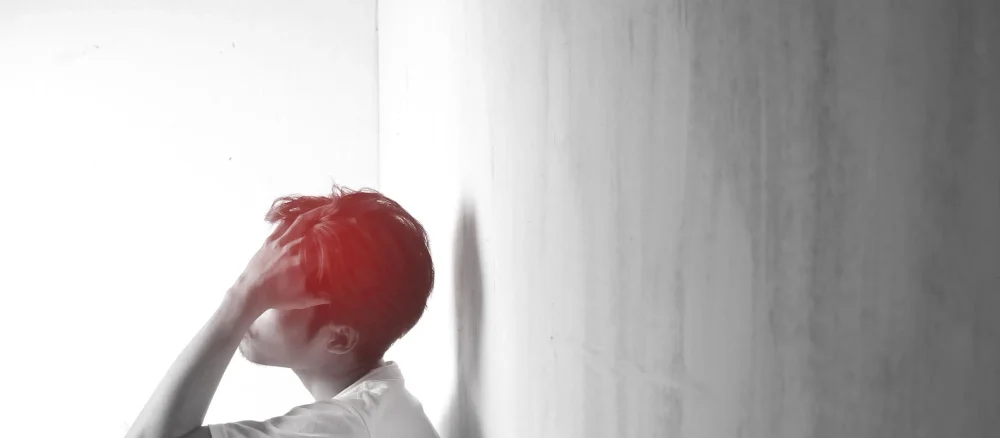 A teenage man with headaches and migraines Man sitting and holding head in indoor room with blurred