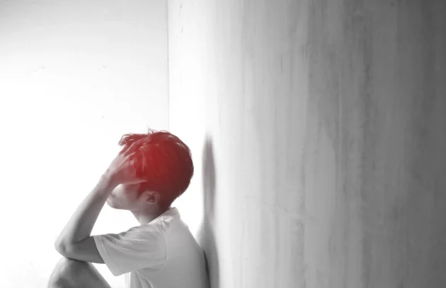 A teenage man with headaches and migraines Man sitting and holding head in indoor room with blurred